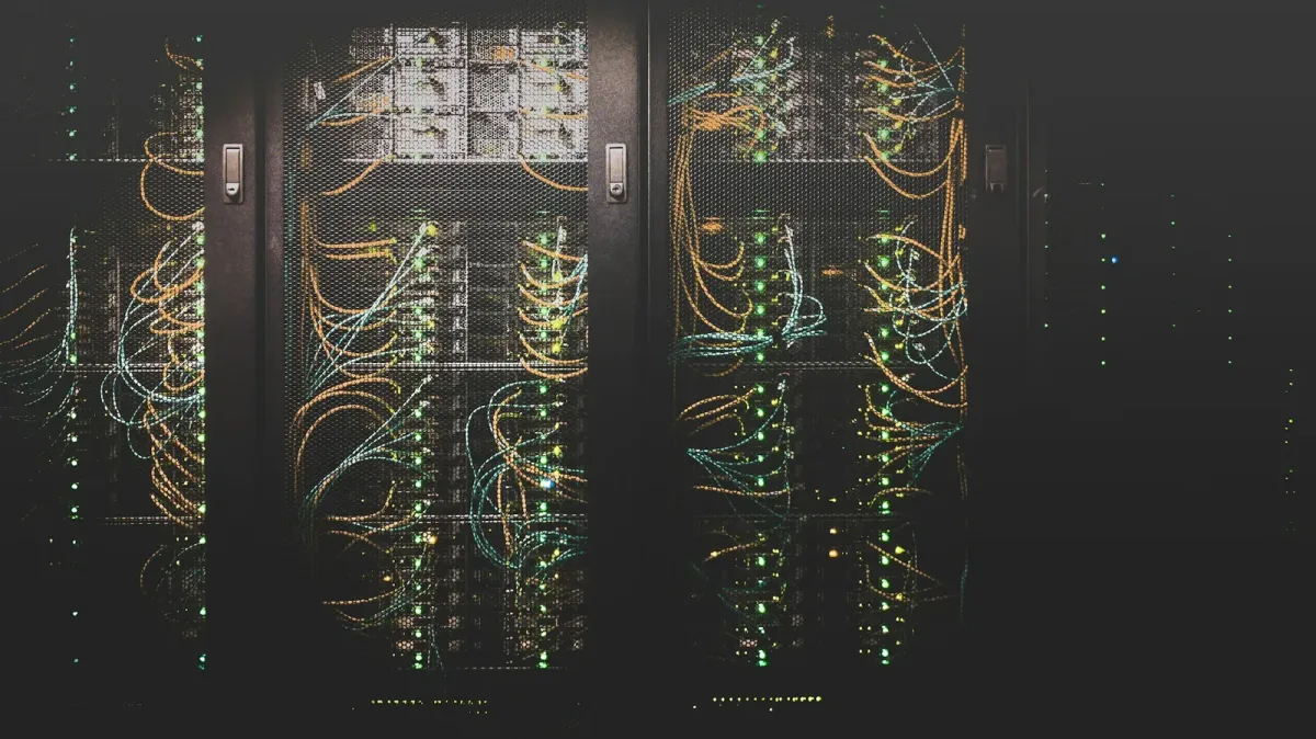 Dunkler Serverraum mit Racks voller Netzwerkkabel und grün leuchtender Status-LEDs