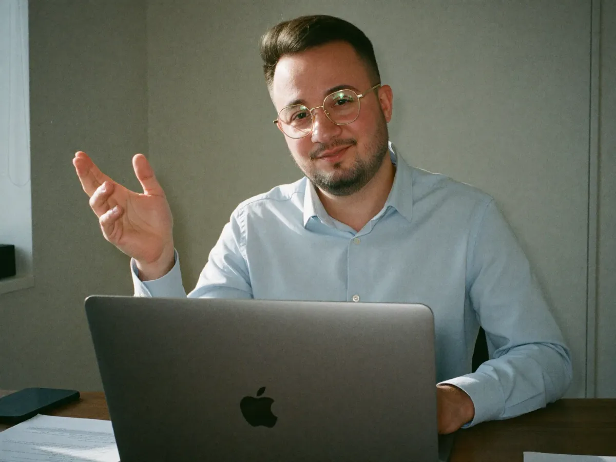 Dominik De Marco am Schreibtisch hinter dem aufgeklappten Notebook, die Hand zu einer erklärenden Geste erhoben
