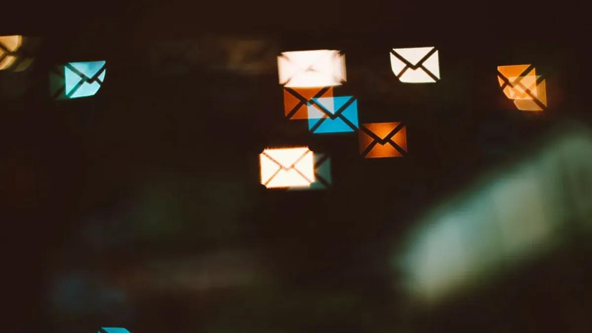Unscharf leuchtende Briefumschlag-Symbole in Weiß, Blau und Orange schweben vor dunklem Hintergrund