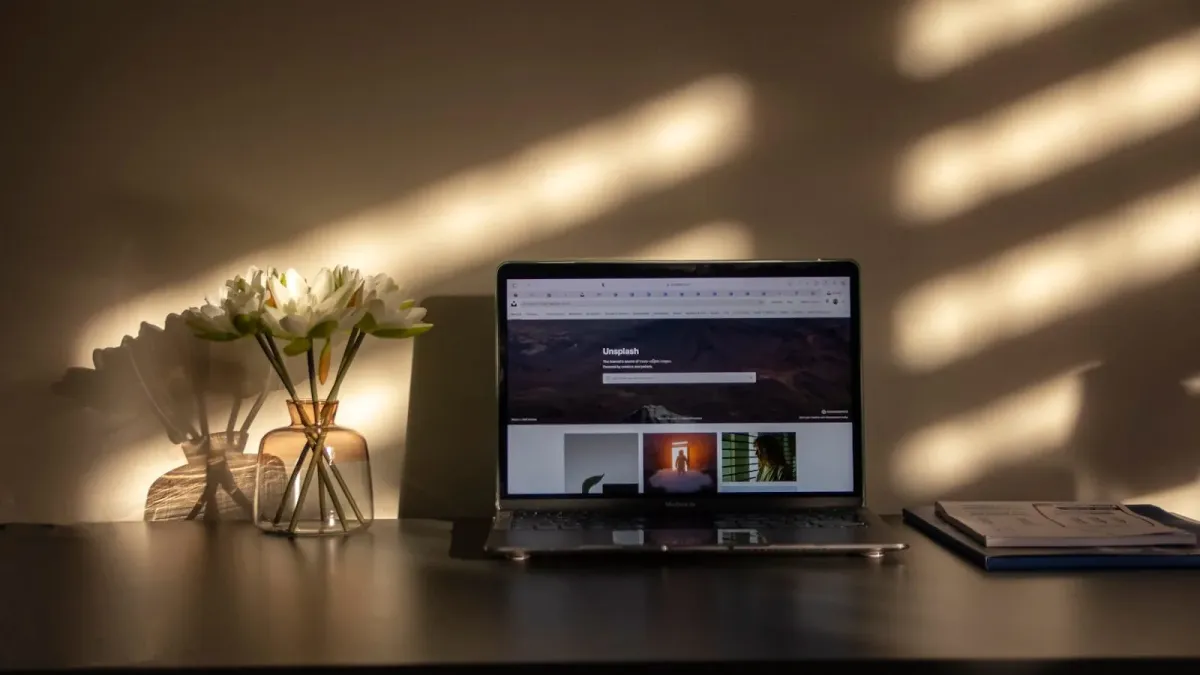 Laptop auf einem Schreibtisch im Abendlicht, im Browser eine Bilddatenbank, Jalousienstreifen an der Wand