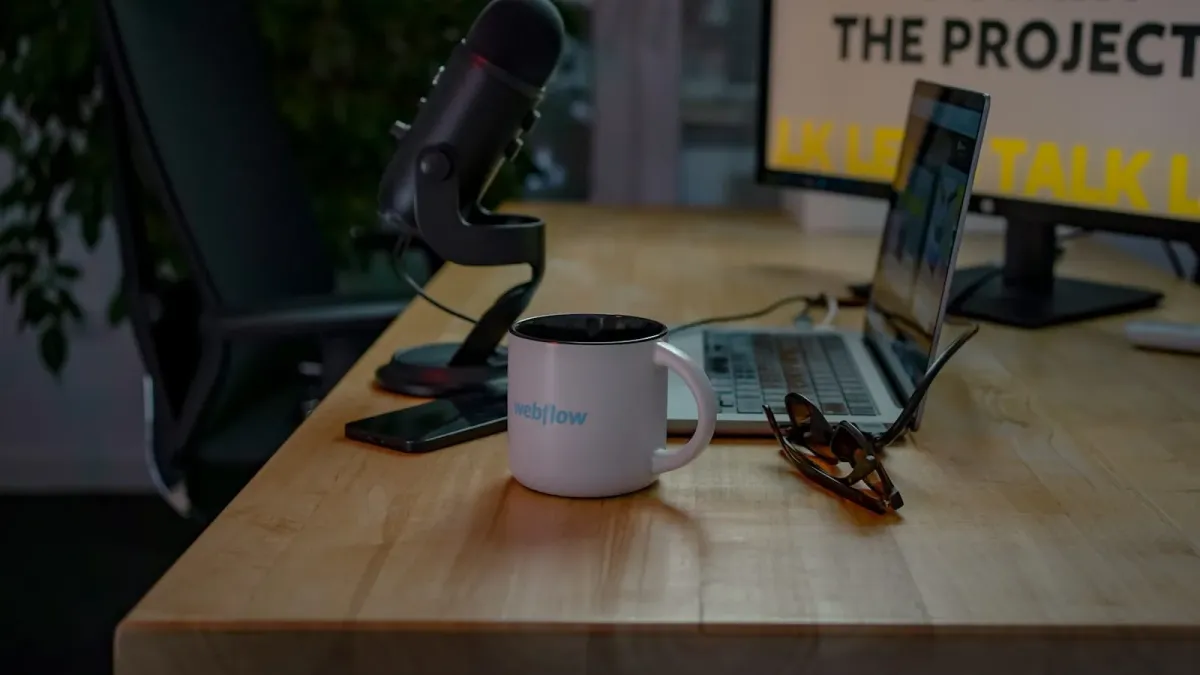Weiße Tasse mit Webflow-Logo auf einem Holzschreibtisch, dahinter Podcast-Mikrofon, aufgeklappter Laptop und Brille