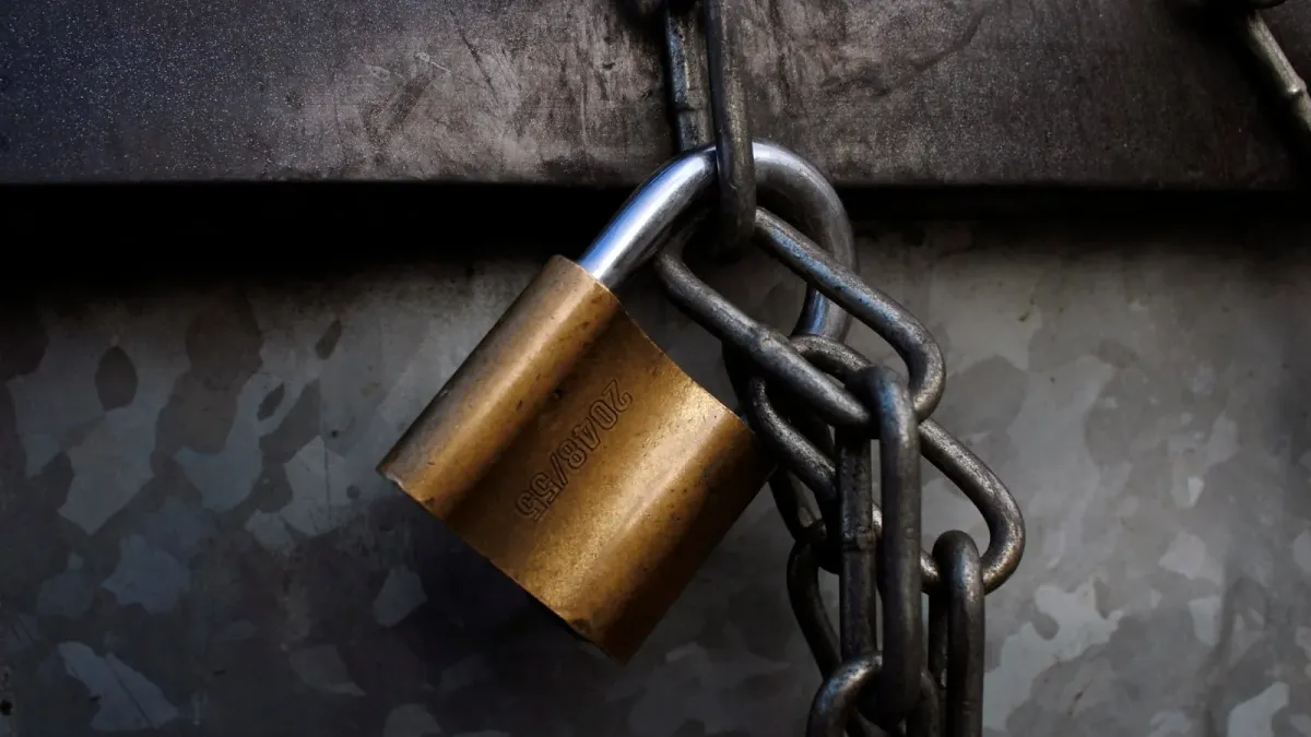 Messing-Vorhängeschloss an einer schweren Stahlkette vor einer verwitterten Metallwand