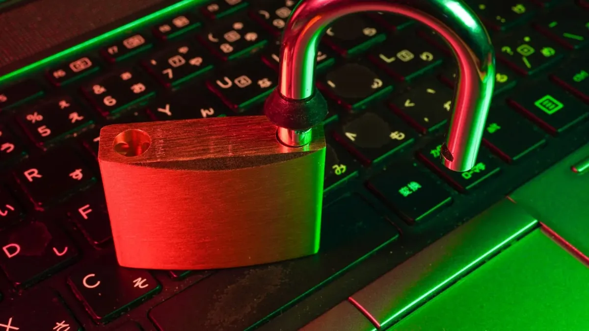 Geöffnetes Vorhängeschloss mit aufgesprungenem Bügel auf einer rot-grün beleuchteten Laptop-Tastatur