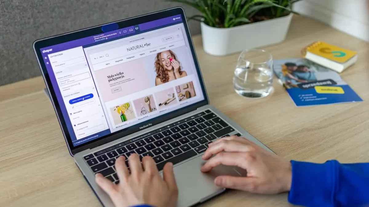 Hände am MacBook, auf dem Bildschirm der Baukasten-Editor eines Onlineshops mit Startseiten-Vorschau
