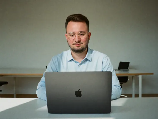 Mann mit Brille im hellblauen Hemd arbeitet am aufgeklappten MacBook in einem hellen, leeren Büro