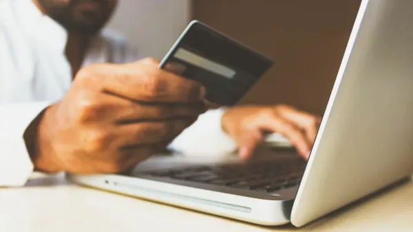 Person hält eine Bankkarte in der Hand und tippt dabei auf der Tastatur eines Laptops