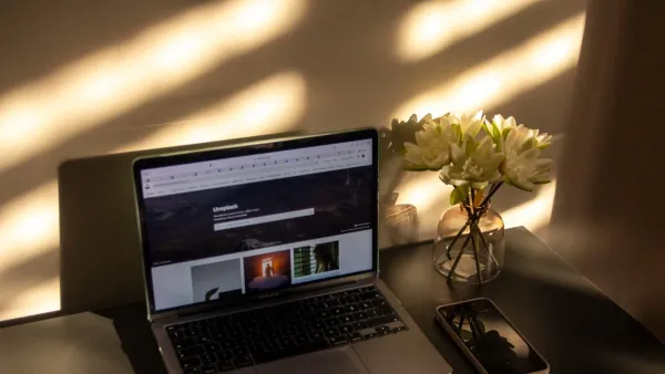 Aufgeklappter Laptop mit geöffneter Website im Browser auf einem Tisch, daneben Blumenvase und Smartphone im Abendlicht