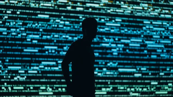 Silhouette eines Mannes vor einer raumhohen Wand aus blau leuchtenden Datenzeilen