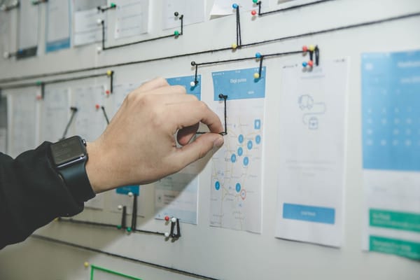 Hand pinnt App-Entwürfe an eine Planungswand, die Stationen sind mit schwarzen Fäden verbunden
