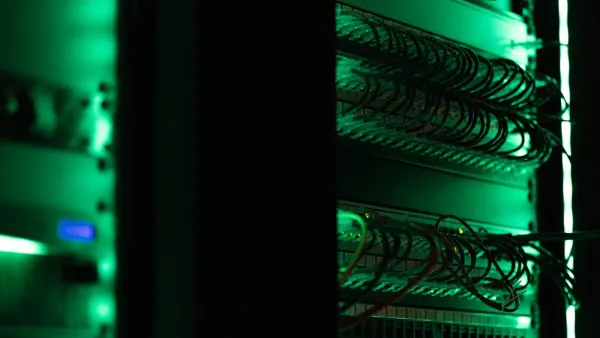 Grün beleuchteter Netzwerkschrank mit Patchfeldern und dicht gesteckten Netzwerkkabeln im dunklen Raum