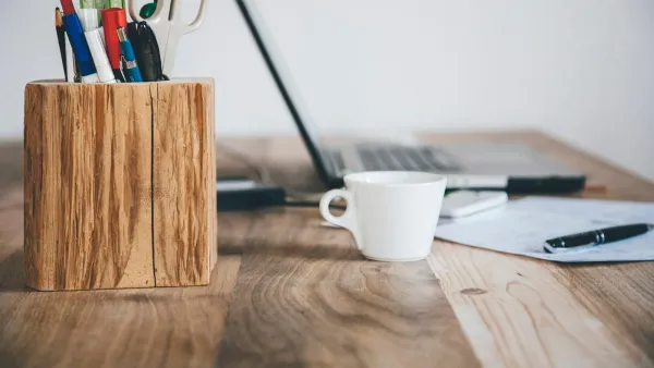 Holzschreibtisch mit Stiftebecher, Espressotasse, aufgeklapptem Laptop und einem Blatt mit Kugelschreiber