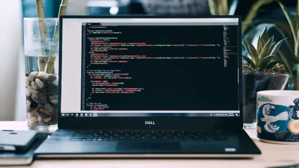 Aufgeklapptes Notebook auf einem Holzschreibtisch, auf dem Bildschirm JavaScript-Code in einem dunklen Editor